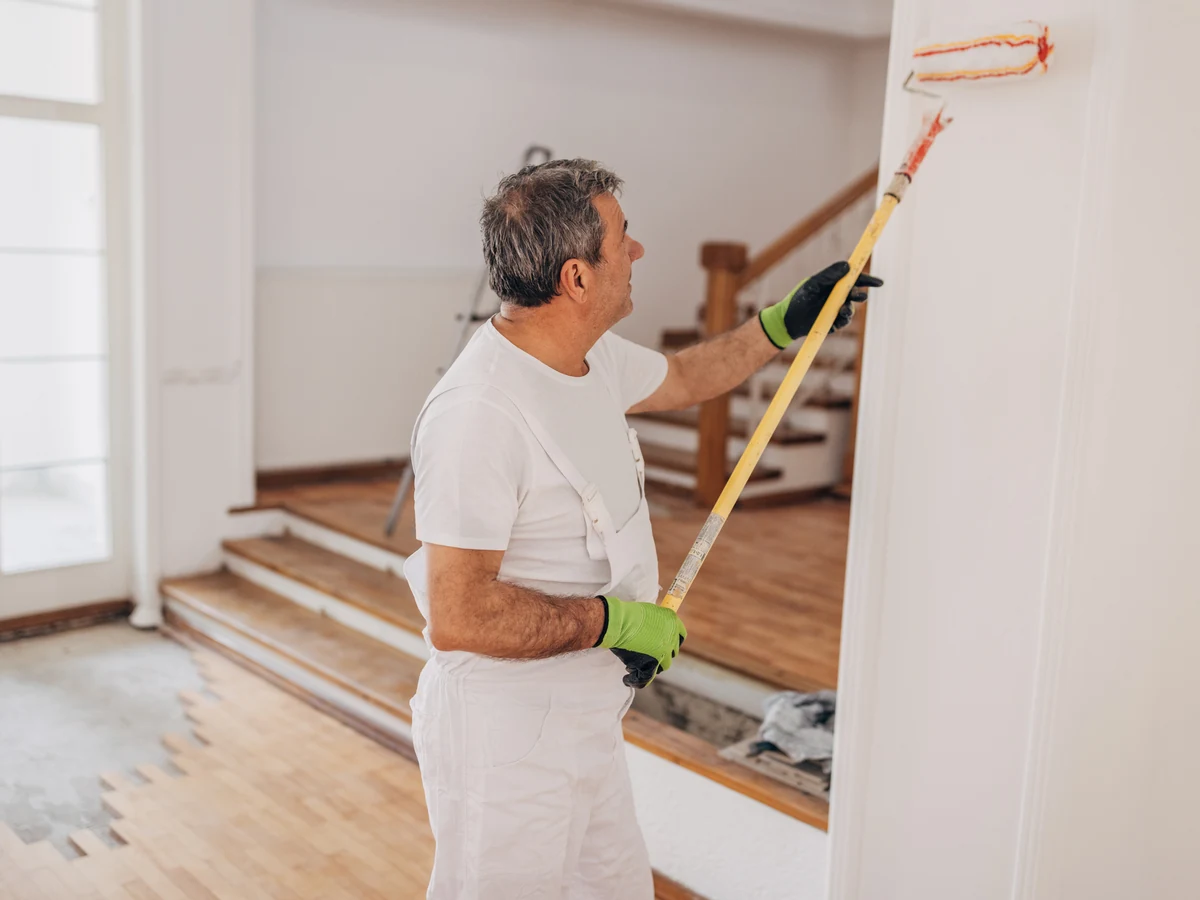 painting-decorating-mature-painter-rolling-bradford-decorators A painter using a long roller on a wall beside a staircase